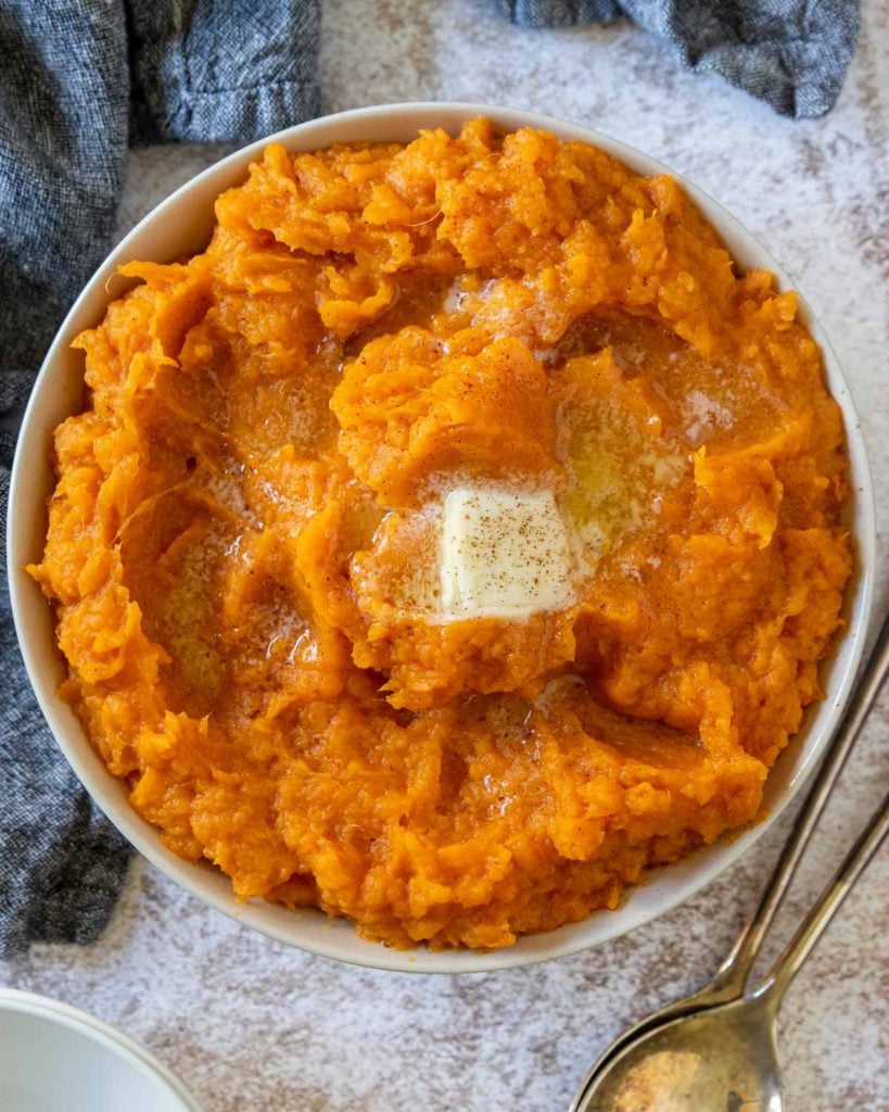 a large bowl of mashed sweet potatoes topped with butter and sprinkled with cinnamon