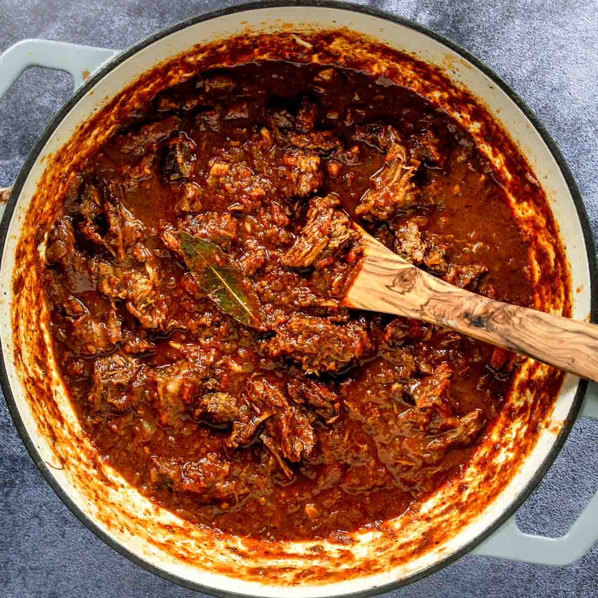 Dutch Oven with Beef Ragu and a wooden spoon