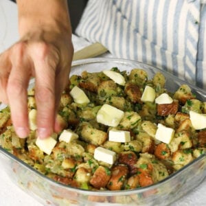 holiday stuffing in a butter dish, a hand placing butter cubes over top