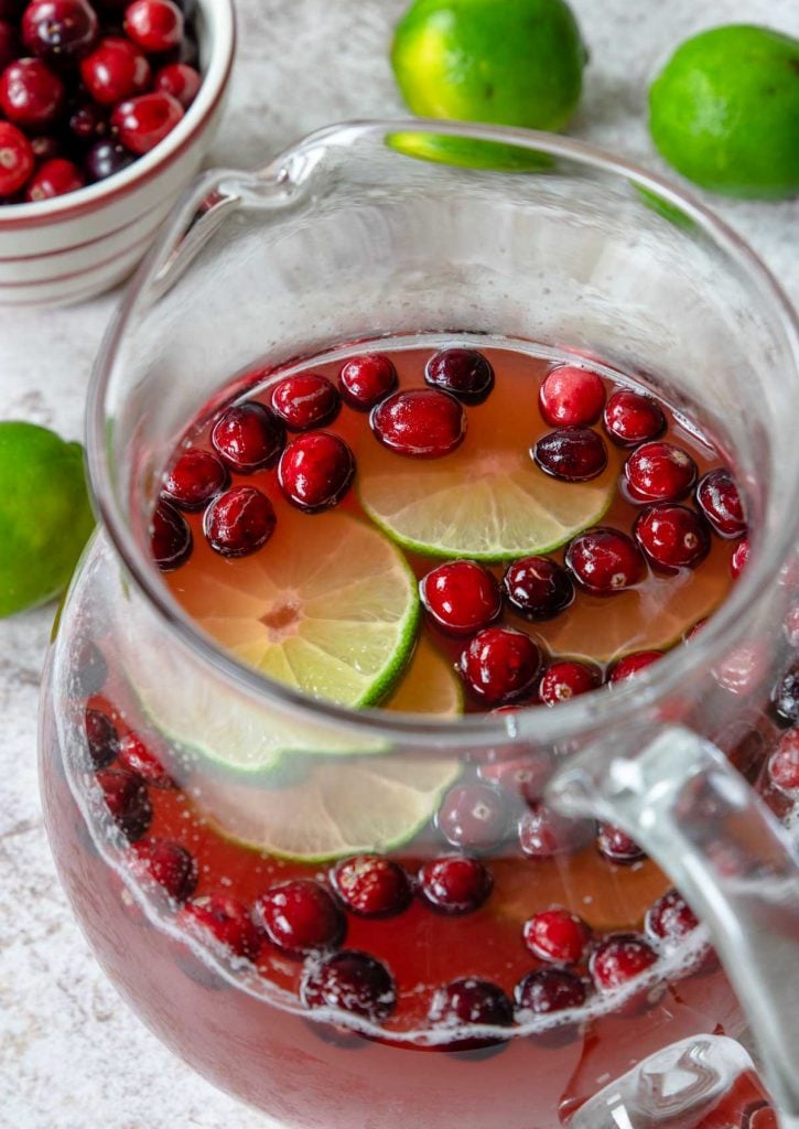 a pitcher of cranberry punch garnished with cranberries and limes