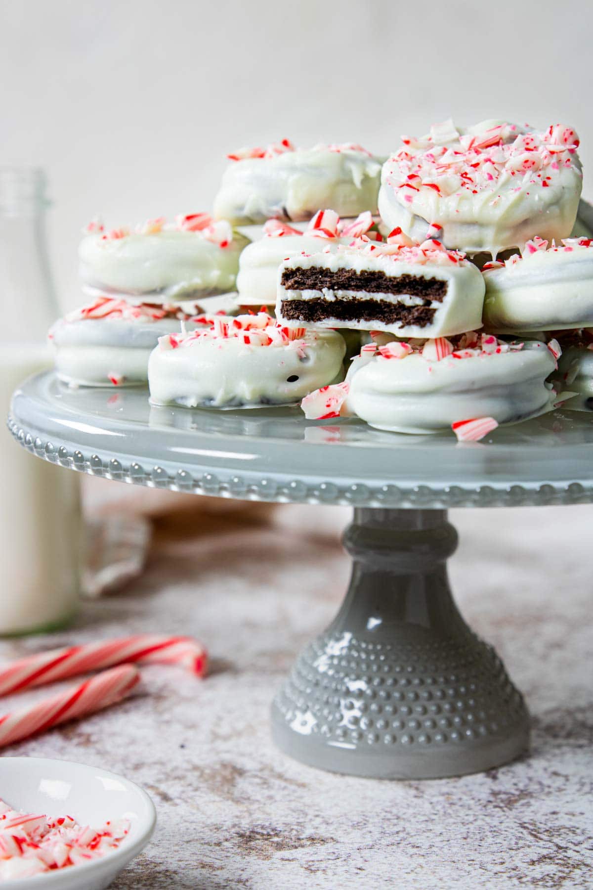white chocolate covered oreos with crushed candy canes on top sitting on a glass cake plate