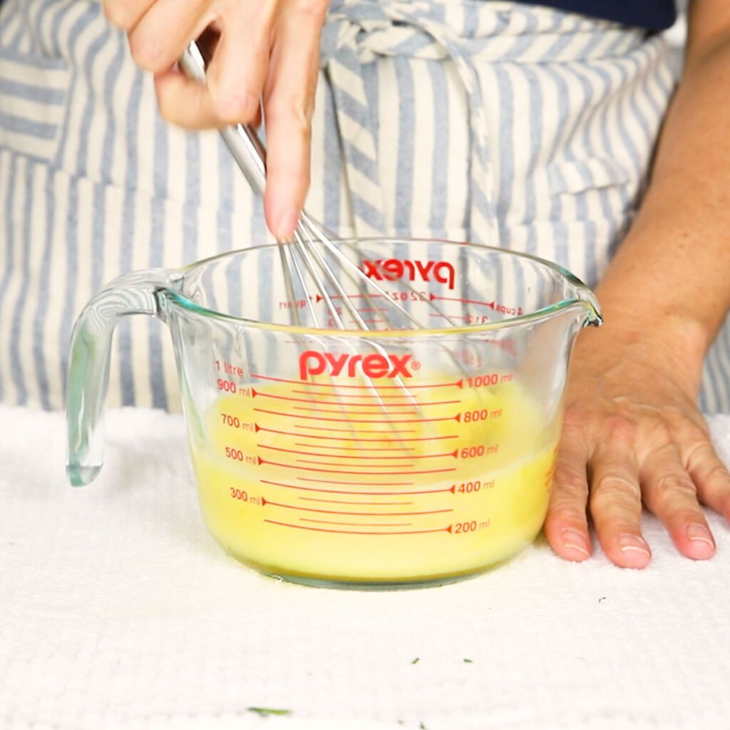 two eggs and chicken broth being whisked together 