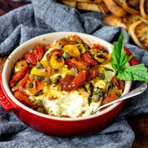 feta cheese that has been baked in a red baking dish, topped with tomatoes and garlic