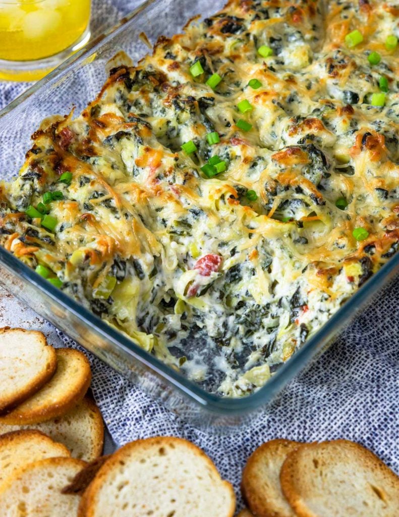 Spinach artichoke dip in a baking dish with bagel chips for dipping