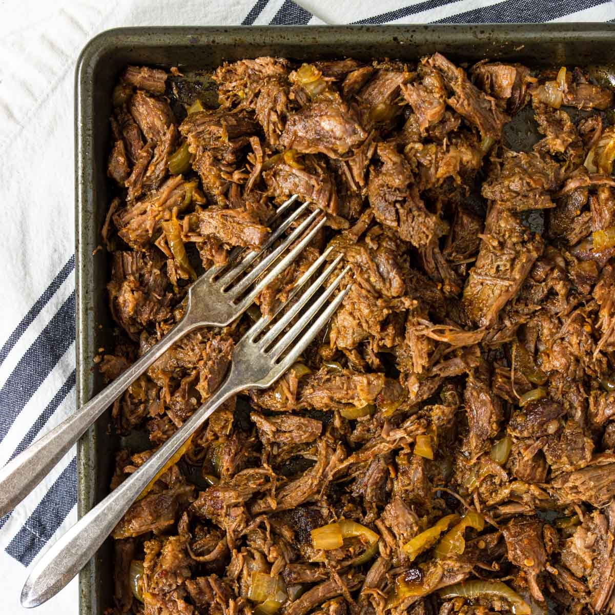 barbacoa on a baking sheet with two forks