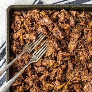 Mexican Shredded Beef Barbacoa on a baking sheet with two forks