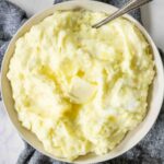 A large serving bowl of Yukon Gold Mashed Potatoes topped with melting butter