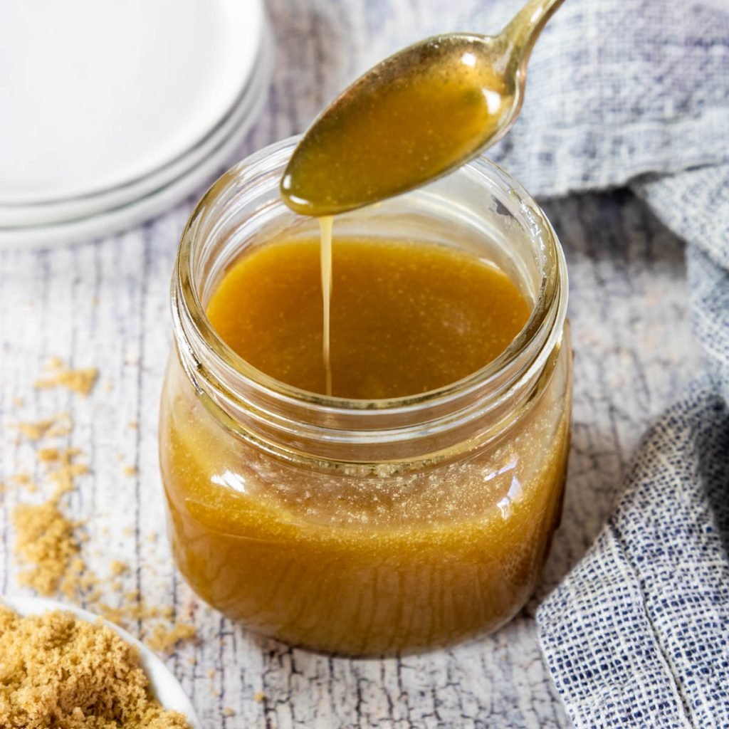 a jar of butter rum sauce being drizzled with a spoon