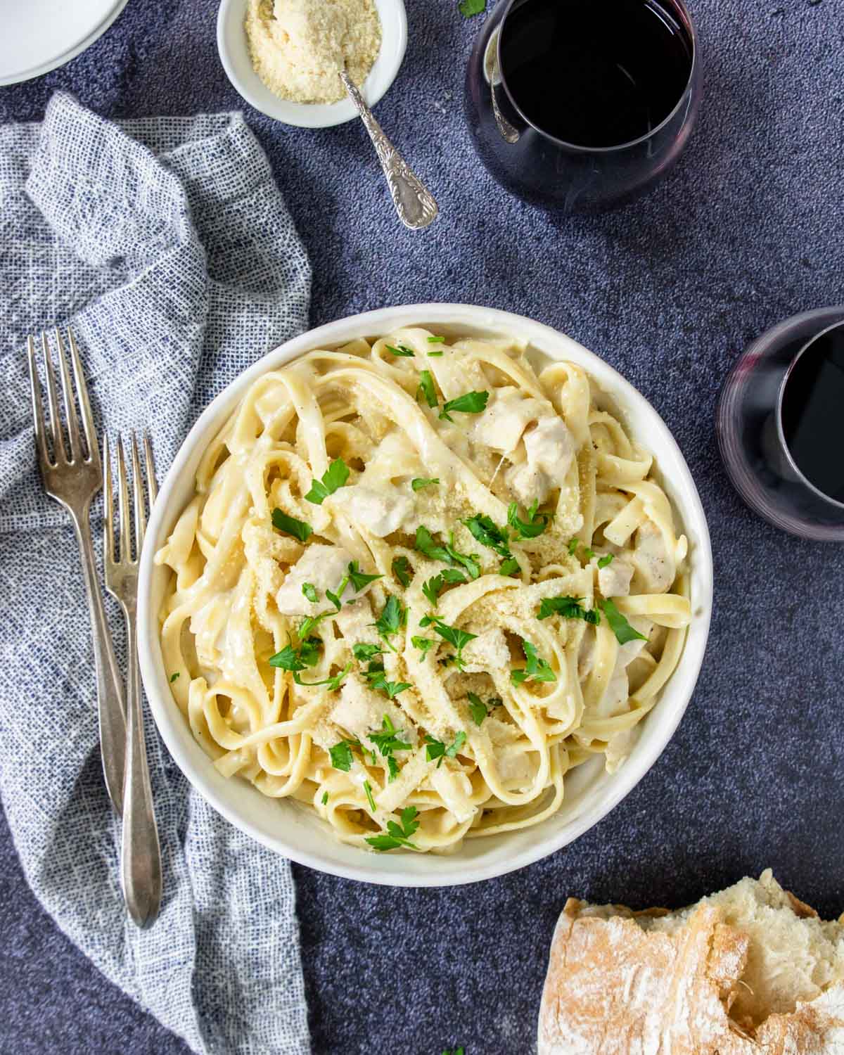 a table with red wine, crusty bread and a bowl of instant pot chicken alfredo