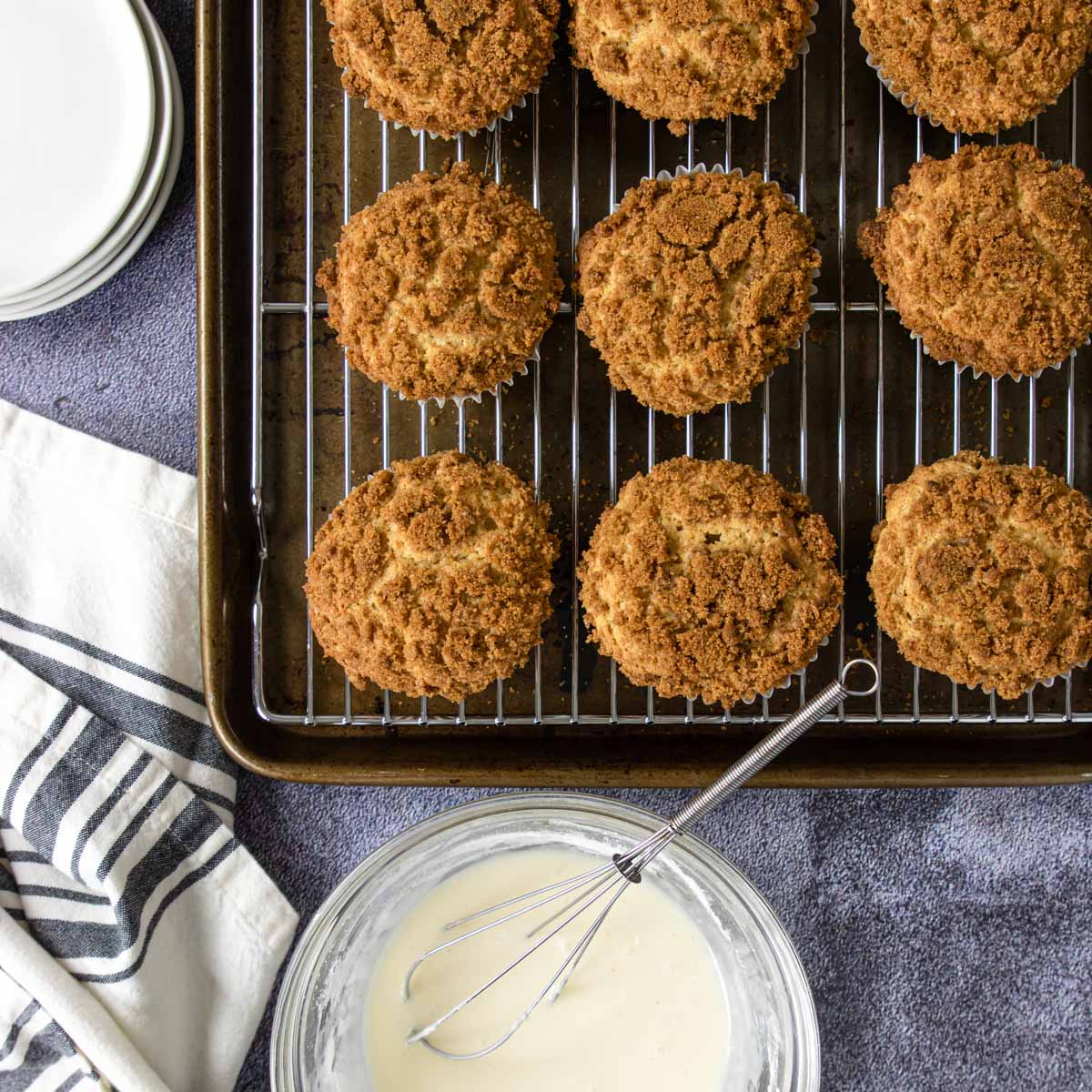 baked muffins on a cooling rack with a bowl of vanilla glaze 