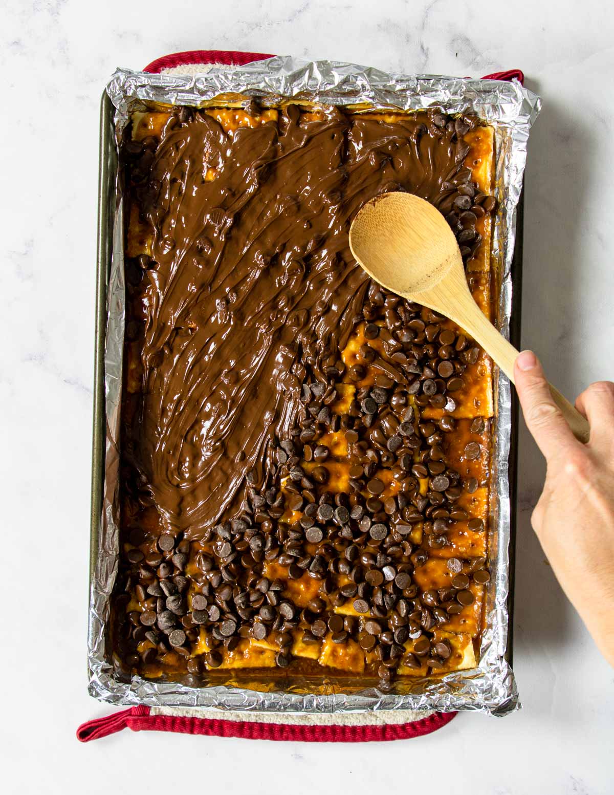 chocolate chips being spread on top of saltine toffee