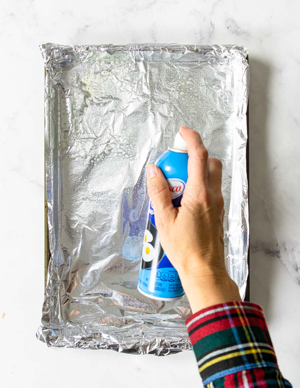 foil covered baking sheet being sprayed with baking spray