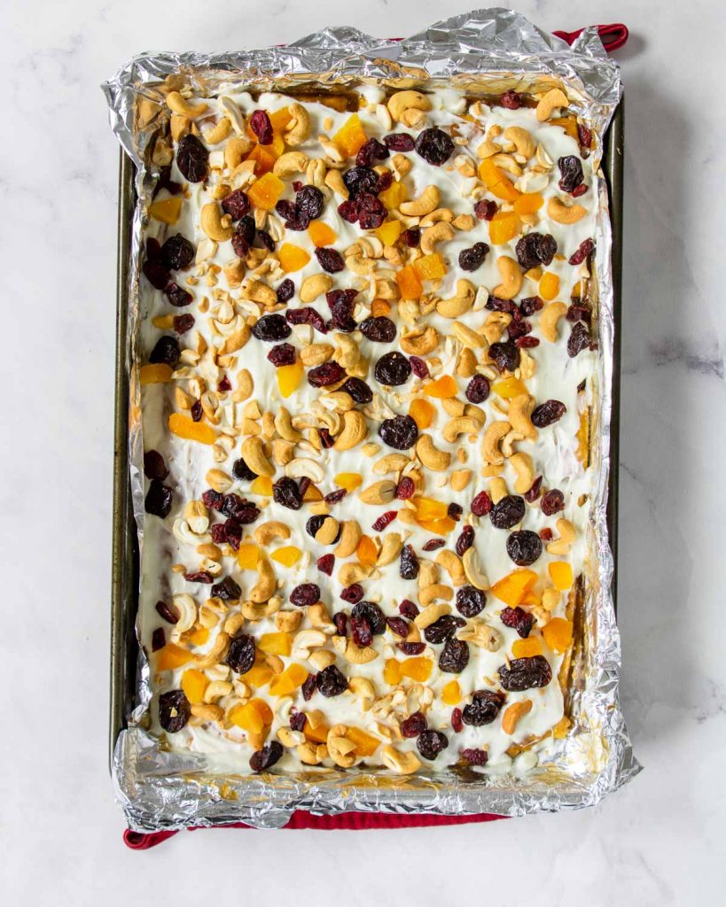 white chocolate toffee in a baking sheet topped with cashews and dried fruit