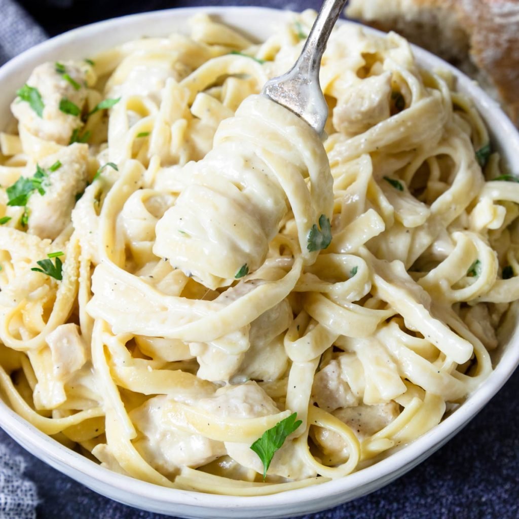 a white bowl of the very best chicken alfredo that is creamy and cheesy, being twirled on a fork
