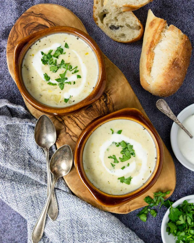 two bowls of potato leek soup with parsley and bread