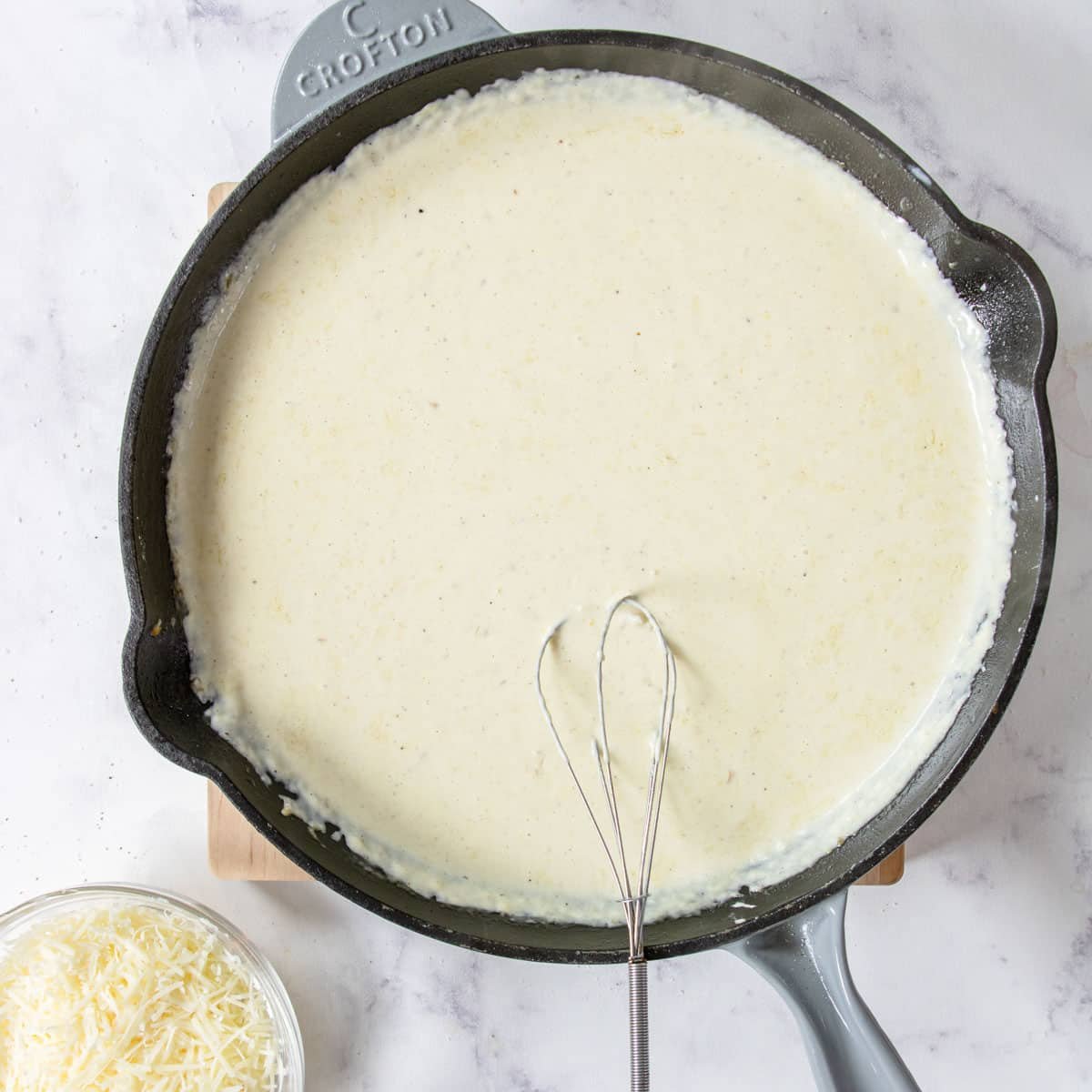 Alfredo sauce being made in a skillet with a whisk.