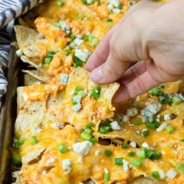 buffalo chicken nachos with toppings being grabbed by a hand