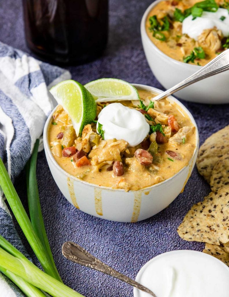 a bowl of chicken chili topped with sour cream and limes