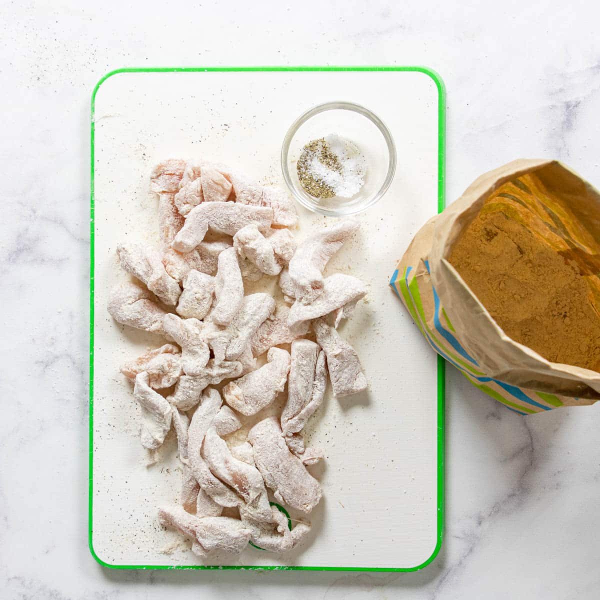 chicken on a cutting board seasoned with salt and pepper and tossed in flour. 