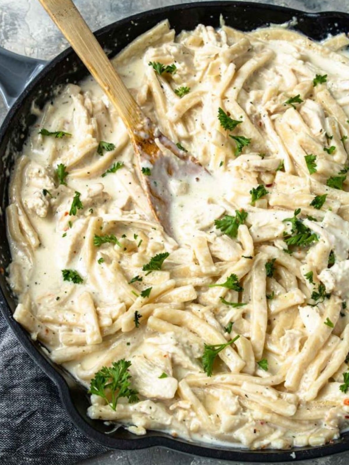 creamy chicken and noodles in a pan with a wooden spoon