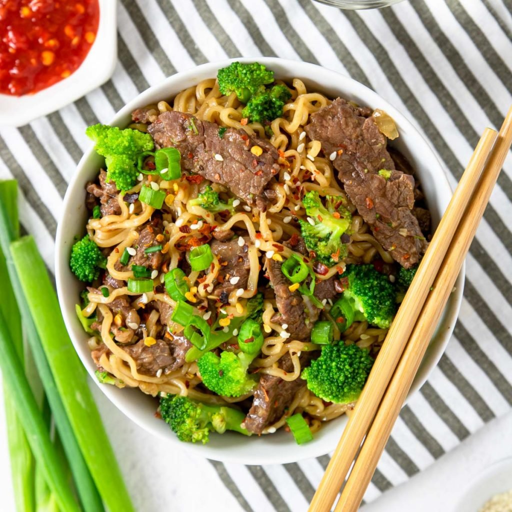 a bowl of ramen with beef and broccoli green onions and chop sticks
