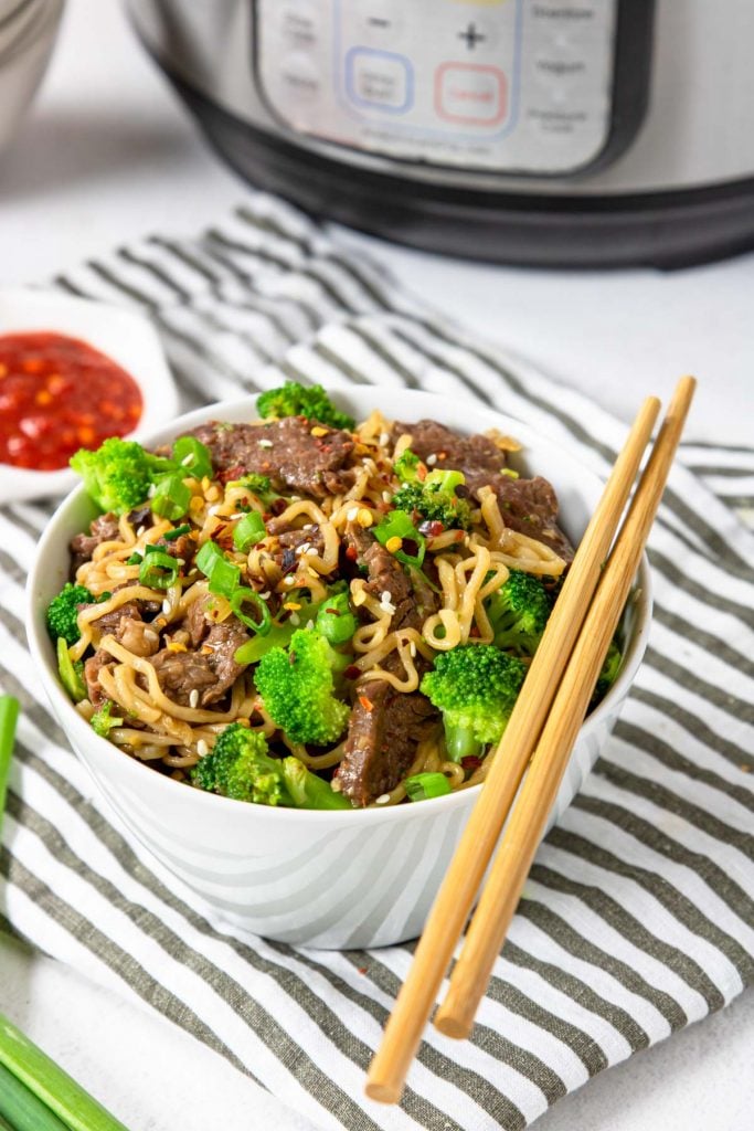 a bowl of beef ramen with broccoli and a pair of chop sticks