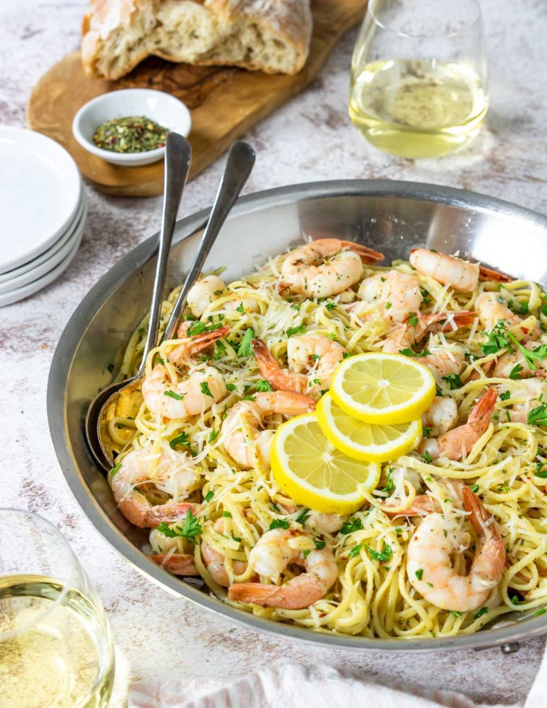 a dinner table with a skillet of shrimp scampi linguine, bread, and white wine