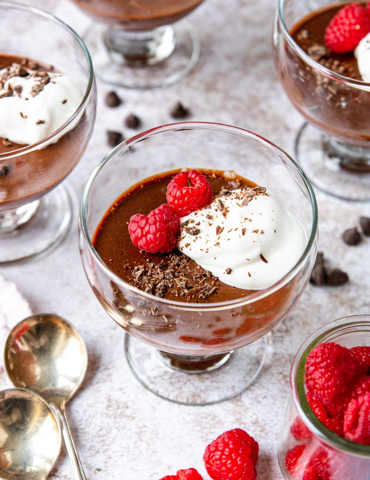 a dessert cup full of chocolate pot de crème topped with whipped cream and raspberries
