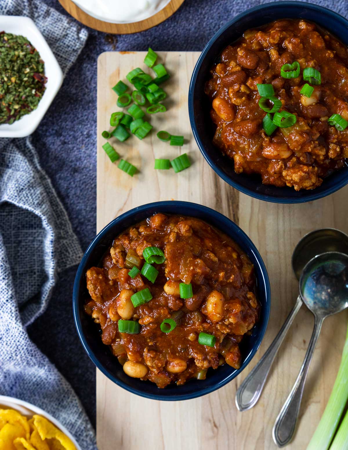 two bowls of chili from above with chili toppings around