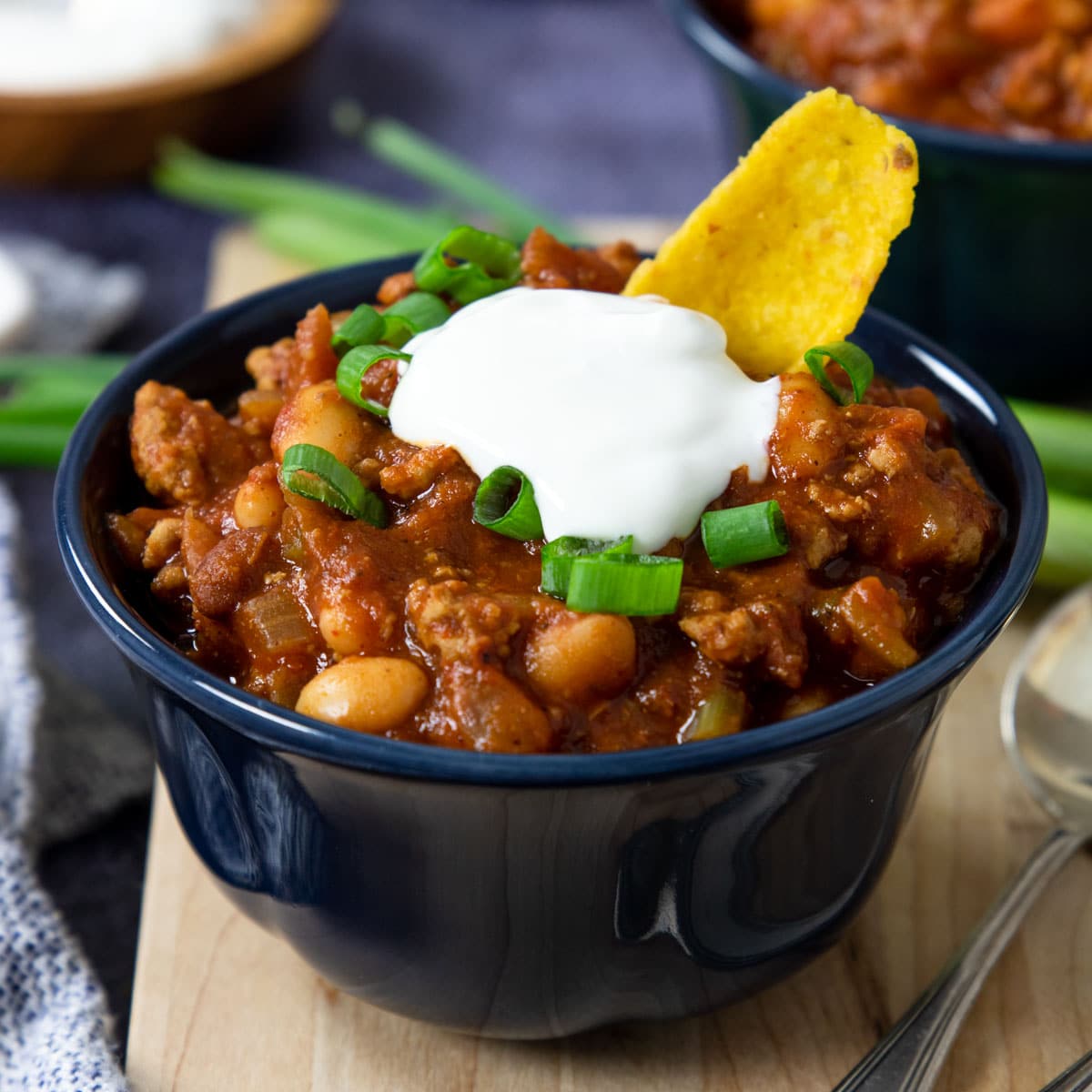 a bowls of chili with turkey topped with sour cream, fritos and green onions