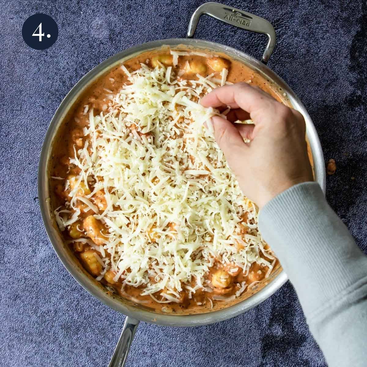 a hand sprinkling mozzarella cheese over gnocchi
