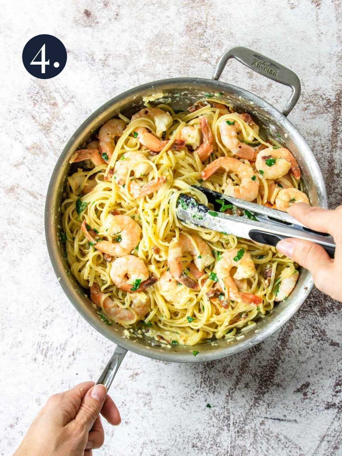 a skillet full of shrimp carbonara pasta being tossed with tongs