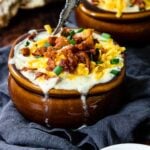 a bowl of creamy soup topped with cheese, bacon and onions