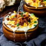 creamy red potato soup topped with bacon and cheese in a brown crock bowl