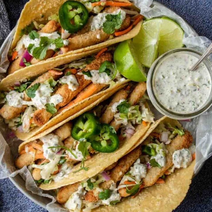 a plate of fish stick tacos topped with tartar sauce