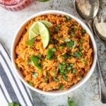mexican rice in a bowl topped with cilantro and limes