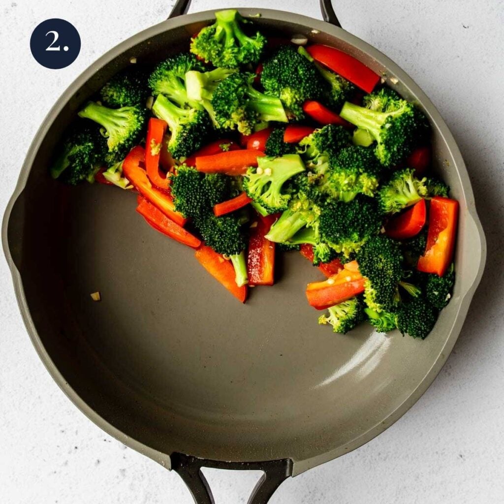 broccoli and red peppers pushed to one side of a non stick skillet