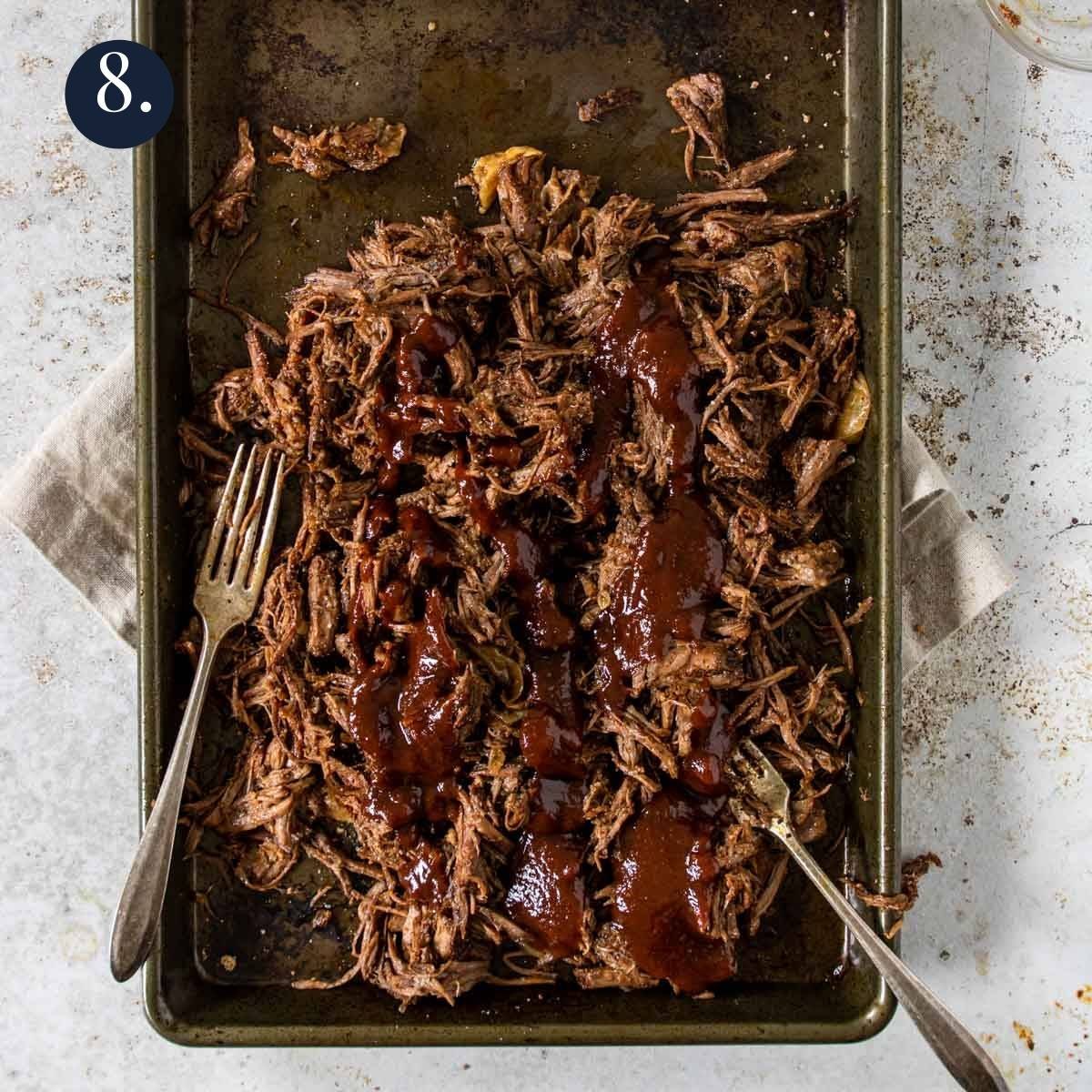 a rimmed baking sheet with shredded beef coated in BBQ sauce