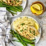 two dinner plates with parmesan tilapia, couscous and asparagus