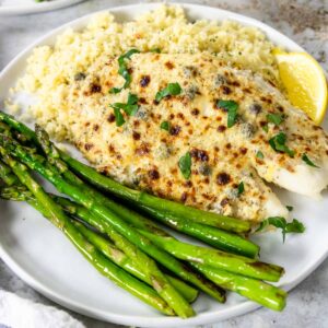 broiled parmesan tilapia on a plate with couscous and asparagus