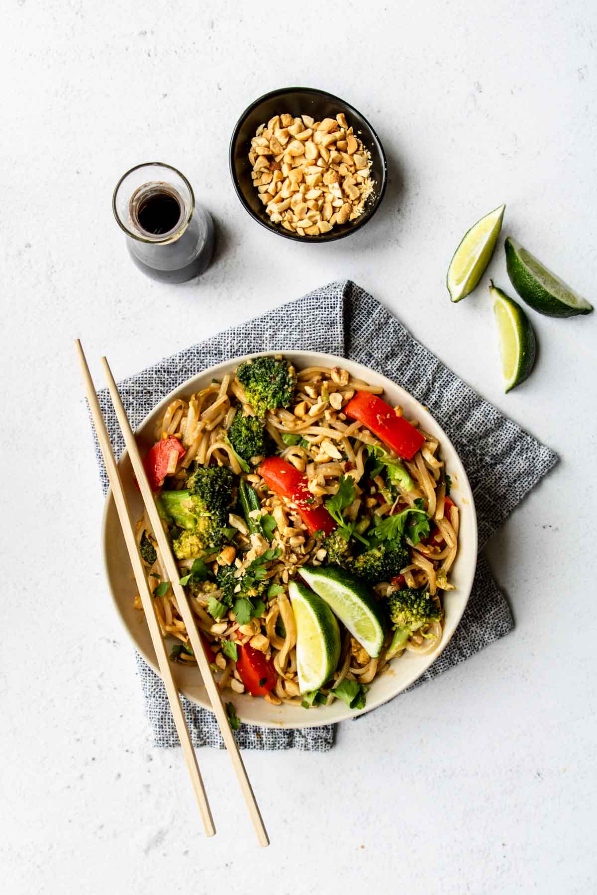 a bowl of Pad Thai with peanuts, limes and soy sauce to the side