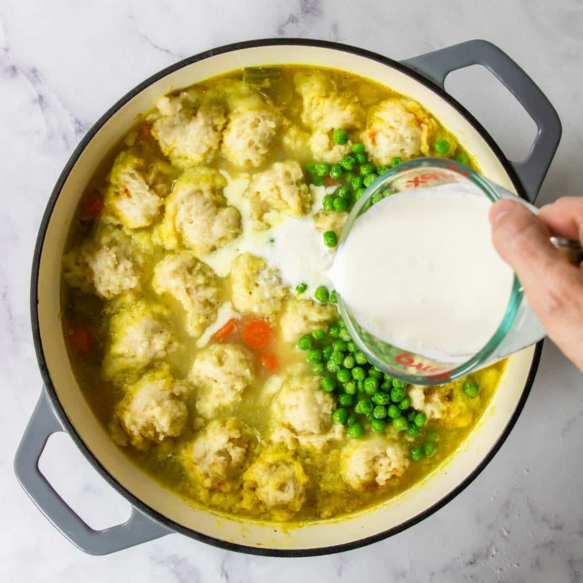 frozen peas and heavy cream being added to chicken and dumplings