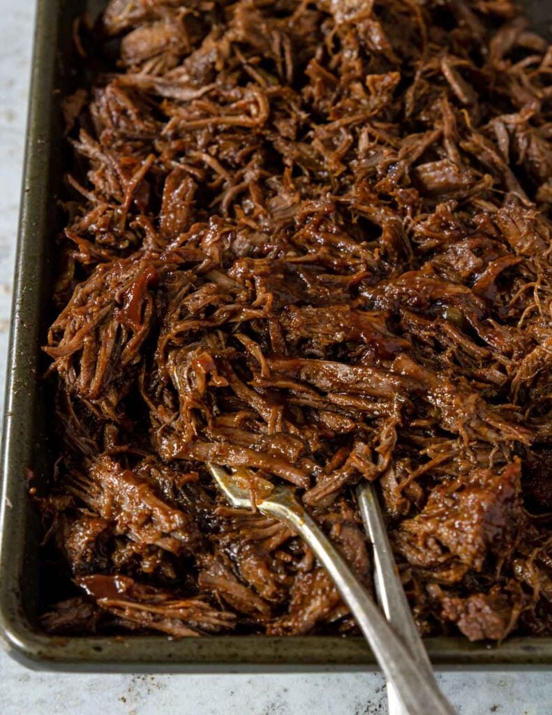a rimmed baking sheet with shredded beef coated in seasoning and BBQ sauce
