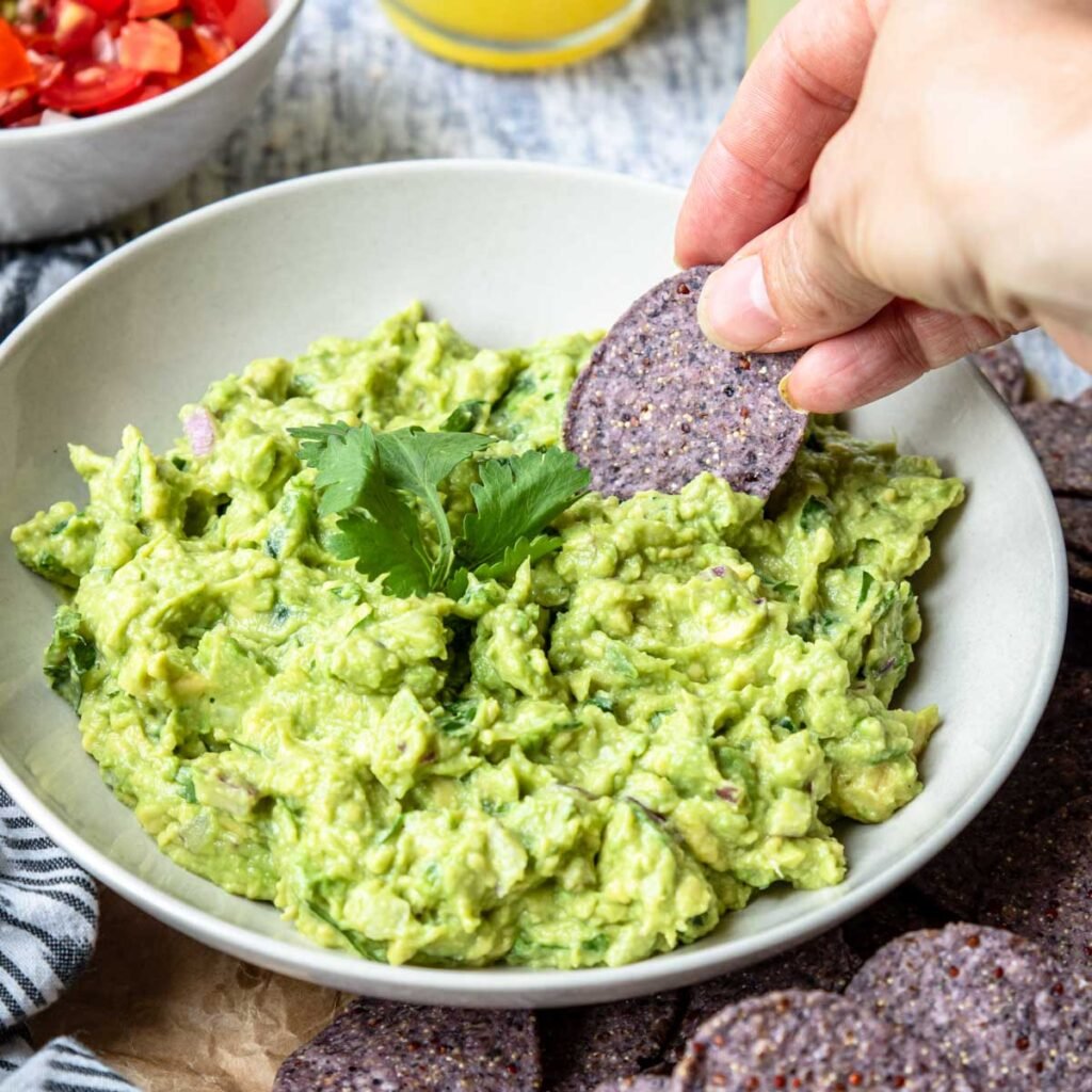 a bowl of fresh avocado guacamole with a chip dipping in