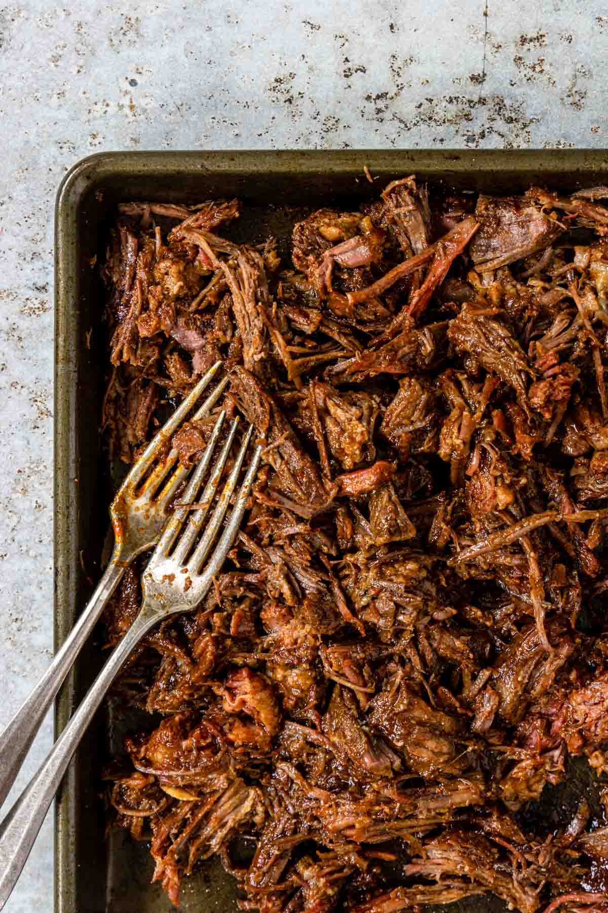 a baking pan with shredded BBQ beef and two forks