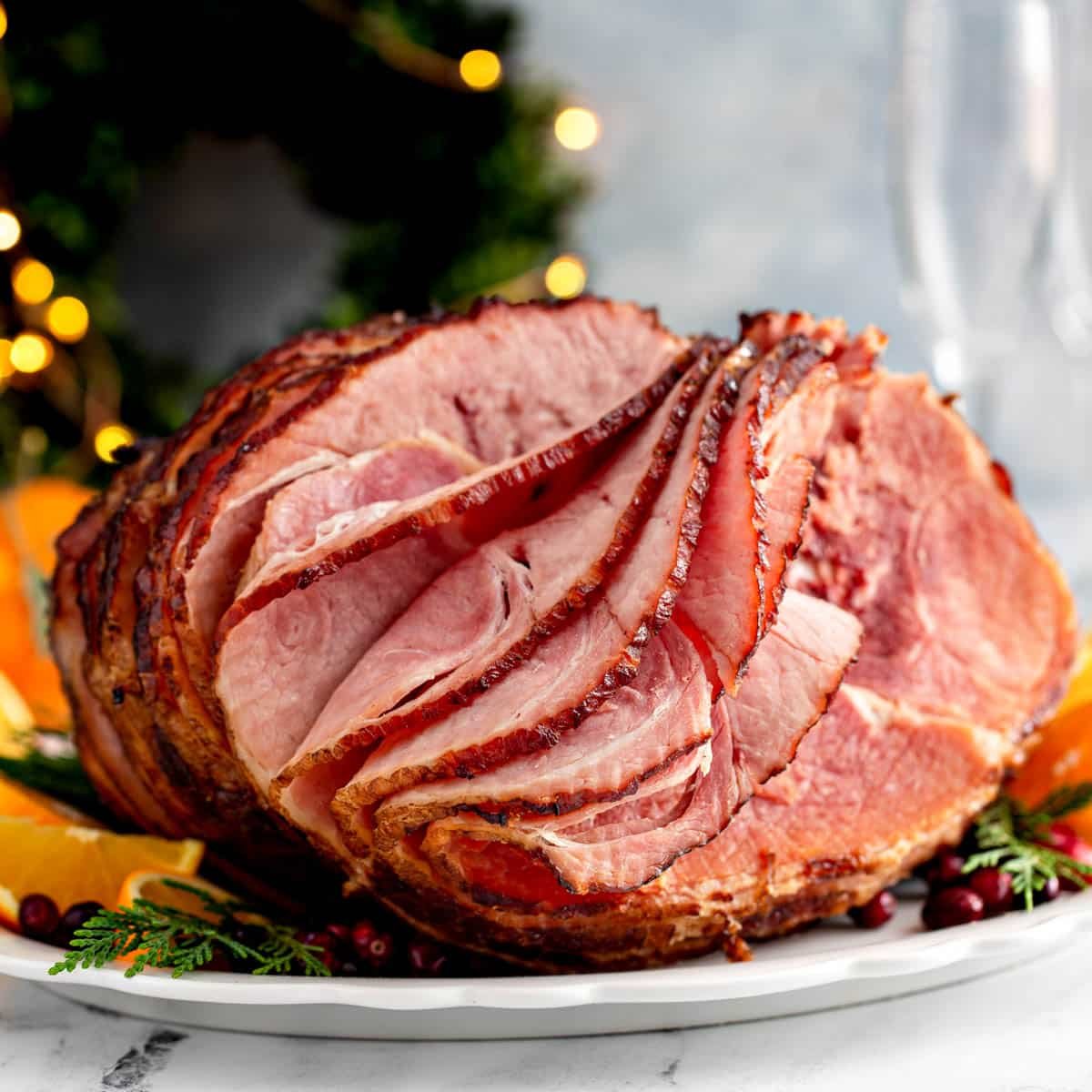 a large holiday ham on a plate with oranges and greenery