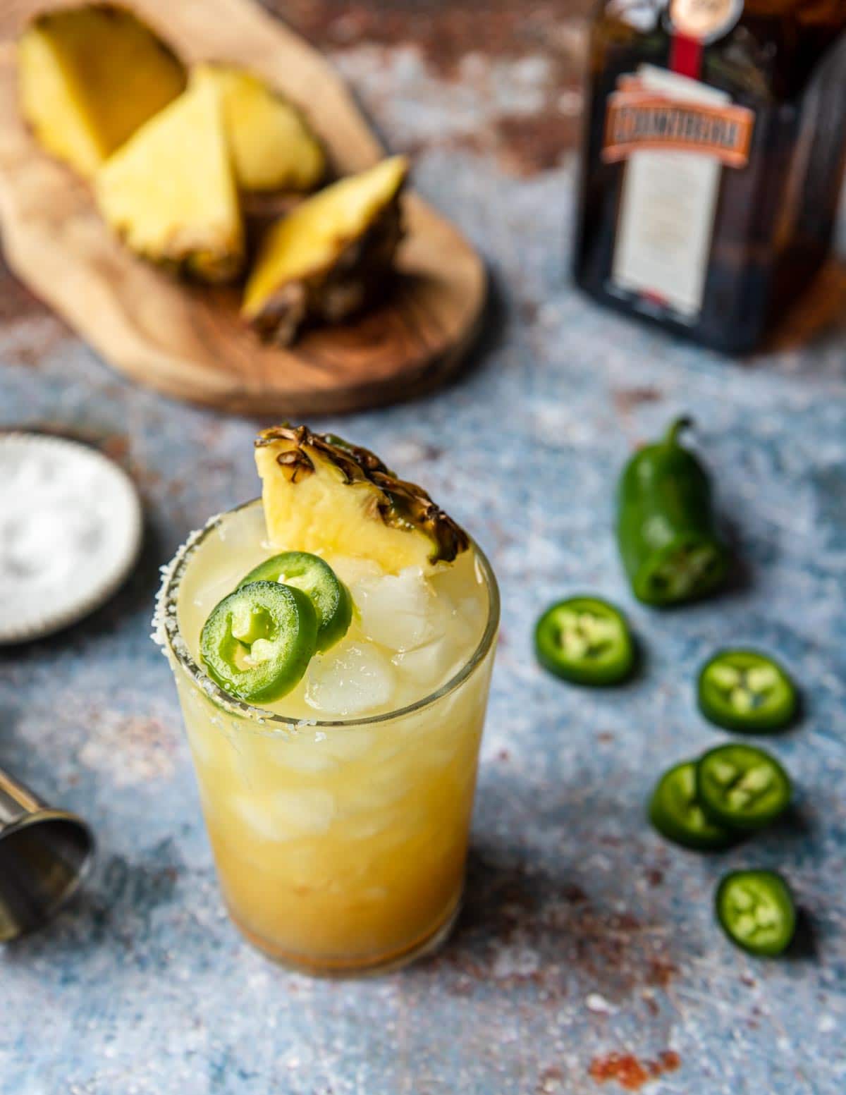 a glass of pineapple jalapeno margarita garnished with pineapple and jalapeno