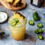 pineapple jalapeno spicy margarita in a glass with jalapenos to the side