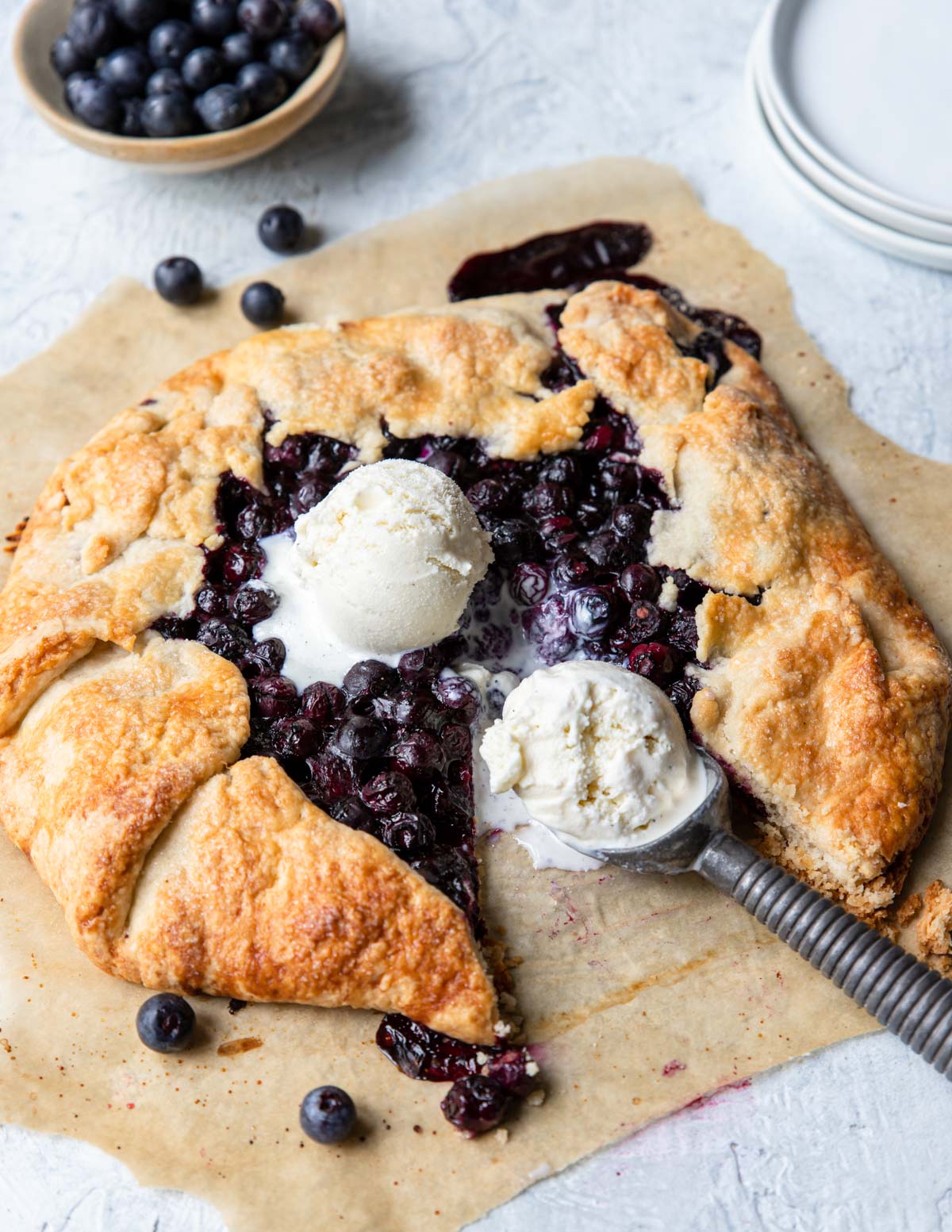 A blueberry galette on parchment paper with 2 scoops of ice cream