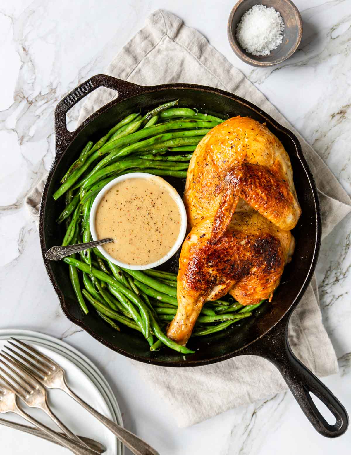 cast iron skillet with a golden roasted half chicken, green beans and gravy